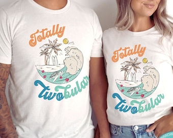 May include: Two white t-shirts with a graphic of a beach scene and the text "Totally Two-bular".