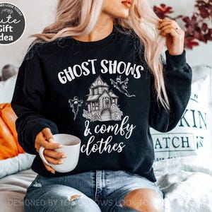 May include: Black sweatshirt with a white graphic of a haunted house and ghosts. The text "Ghost Shows & Comfy Clothes" is printed on the sweatshirt.