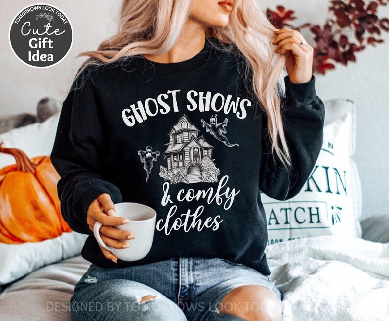 May include: Black sweatshirt with a white graphic of a haunted house and ghosts. The text "Ghost Shows & Comfy Clothes" is printed on the sweatshirt.