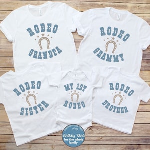 May include: Set of five white t-shirts with blue and brown text and a horseshoe graphic. The shirts say "Rodeo Grandpa", "Rodeo Grammy", "Rodeo Sister", "My 1st Rodeo", and "Rodeo Brother".