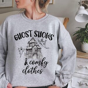 May include: Gray sweatshirt with a black graphic print of a haunted house, ghosts, and the text "Ghost Shows & Comfy Clothes".