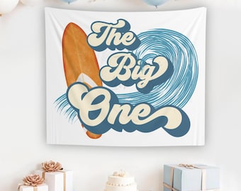 May include: A white banner with blue and yellow text that reads "The Big One". A surfboard with orange and white accents is in the background. The banner is perfect for a first birthday party.