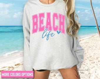 May include: A light gray sweatshirt with the words "BEACH life" in pink and blue. The word "BEACH" is in a bold, block letter font, and "life" is in a script font. A small blue heart is next to the word "life".