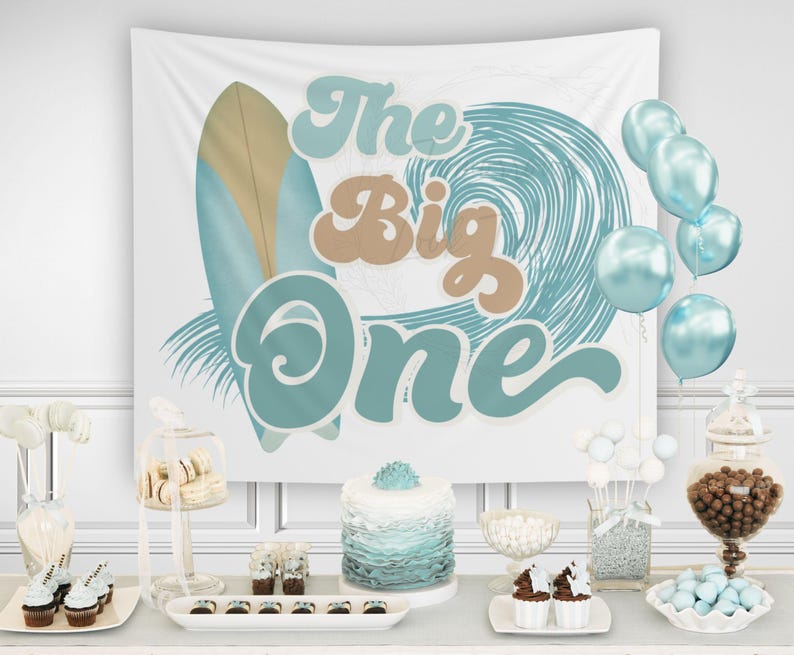 Op de afbeelding: Een feestsc&egrave;ne met een witte achtergrond met een surfboard- en golfontwerp, met de tekst "The Big One". De sc&egrave;ne omvat blauwe ballonnen, een taart, cupcakes en diverse snoepjes, wat een feestelijke sfeer cre&euml;ert.