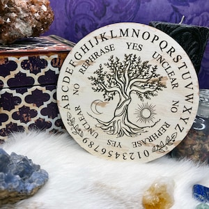 May include: A wooden Ouija board with a tree of life design, featuring the alphabet, numbers 0-9, yes, no, and unclear. The board is surrounded by crystals and a black candle.