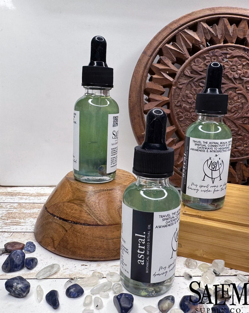 May include: Three glass bottles of green liquid with black dropper tops. The bottles are labelled "astral." The bottles are sitting on a wooden surface with small blue and white stones scattered around them. The text on the bottles reads "astral. Botanical Infused Ritual Oil. Travel the Astral Realm. Spiritual Connectivity. Gateways to Heightened Awareness & Introspective Visions. My spirit soars in the dreaming wisdom from the stars."
