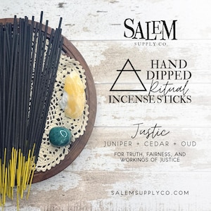 May include: A wooden tray holds a bundle of black incense sticks with yellow tips, alongside crystals and a doily. Text reads "Salem Supply Co." and "Hand Dipped Ritual Incense Sticks". The label says "Justic" with juniper, cedar, and oud.