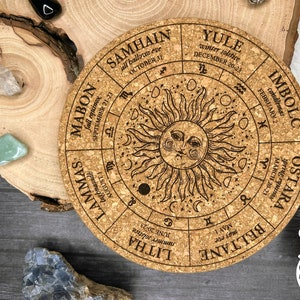 May include: A corkboard wheel with a sun and moon design, featuring the eight major holidays of the Wheel of the Year, including Yule, Samhain, Mabon, Lammas, Litha, Beltane, Ostara, and Imbolc.
