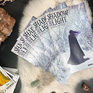 May include: A stack of four magazines with the title "Shadow and Light: A Seasonal Publication for Witches, Wiccans & Pagans" printed on the cover. The cover features a snowy forest scene with a person wearing a black cloak walking through the woods.