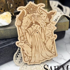 May include: Wooden laser-cut artwork featuring a woman in a flowing gown, flanked by wolves and holding torches. The design includes crescent moons, stars, and a pentacle. The text "SALEM SUPPLY CO." is at the bottom.