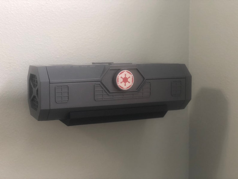 May include: A gray wall-mounted storage box with a black front panel and a red and white Imperial symbol on the top.