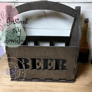 May include: A dark brown wooden beer carrier with a handle and the word "BEER" cut out on the front. The carrier is empty and sitting on a wooden surface.