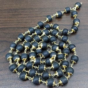 May include: A black and gold beaded necklace with a floral design. The beads are made of a dark material and have a gold trim. The necklace is strung on a gold chain.