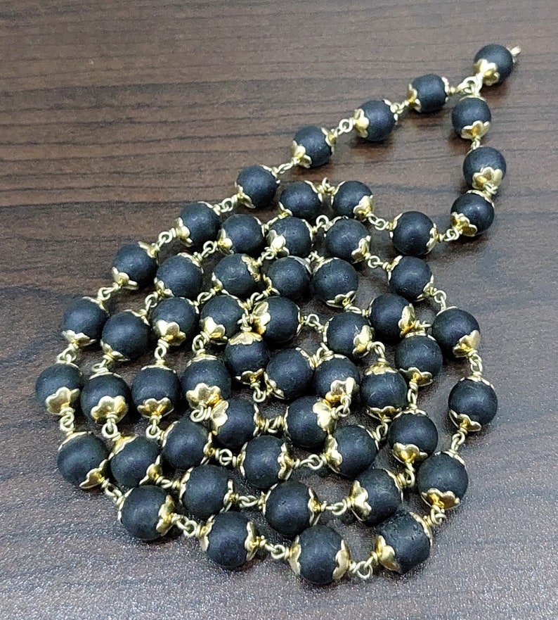May include: A black and gold beaded necklace with a floral design. The beads are made of a dark material and have a gold trim. The necklace is strung on a gold chain.