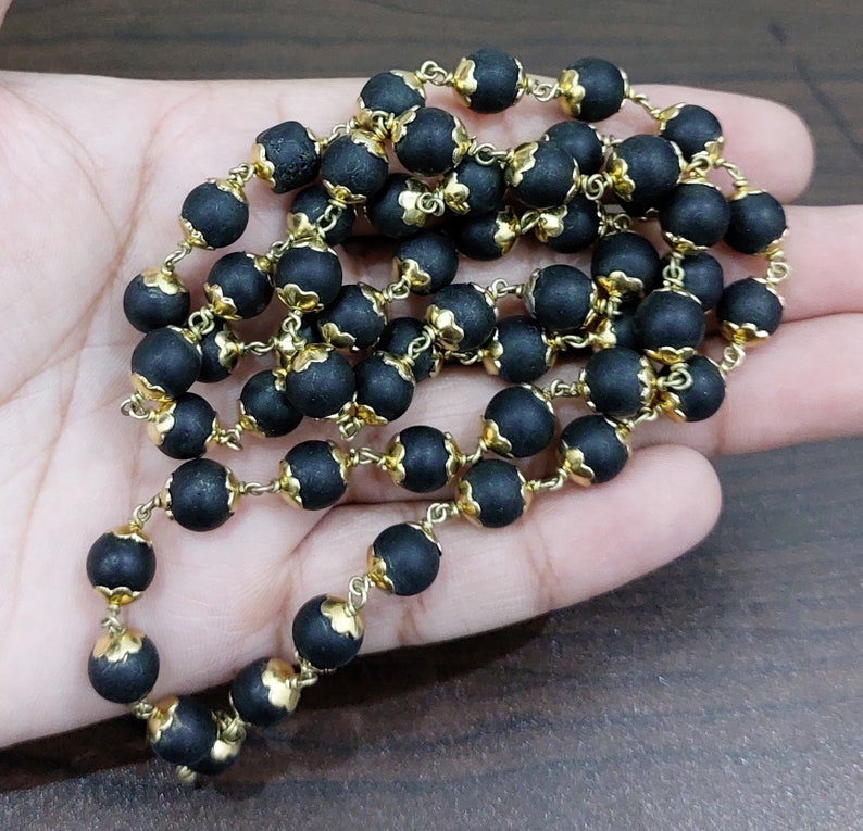 May include: A black beaded necklace with gold accents. The beads are round and have a slightly textured surface. The necklace is strung on a gold chain.