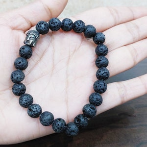 Puede incluir: Pulsera de cuentas de roca volcánica negra con un dije de cabeza de Buda plateado.