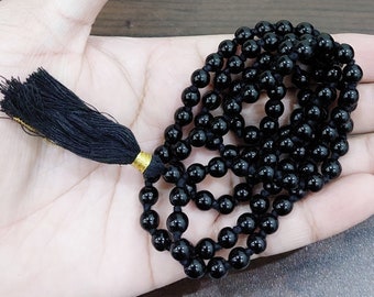 Puede incluir: Un collar mala de cuentas negras con un borla negra. Las cuentas son redondas y lisas.