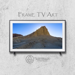 May include: A framed photograph of a desert landscape with a large rock formation in the center. The sky is blue and the sun is setting in the distance. The image is displayed on a television screen with a black frame.