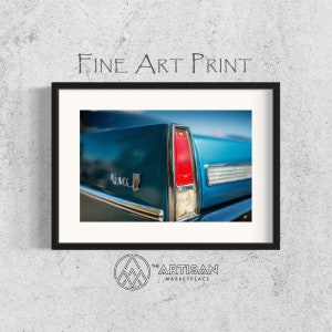 May include: A close-up of the rear taillight of a teal blue classic car. The taillight is red and chrome with a white reflector. The car has a chrome trim and the word "Nova" is visible on the rear panel.