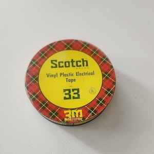 May include: A round roll of Scotch Brand Vinyl Plastic Electrical Tape number 33. The center label is yellow with black text and the 3M logo. The outer edge of the roll features a red, yellow, and black plaid pattern with a green grid overlay.