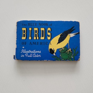 May include: A vintage book titled "The Blue Book of Birds of America" with a blue cover and yellow text. The cover features a yellow and black bird illustration. The book is slightly worn, suggesting it is an antique.