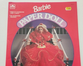 May include: A Barbie paper doll book featuring a red and gold Christmas dress. The cover shows a pre-cut doll and the text "Barbie Paper Doll".
