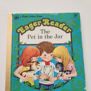 May include: A Little Golden Book Eager Reader book cover with a blue background and green leaves. The title is "The Pet in the Jar". Three children are looking at a jar with a stick insect inside. The book is for early readers.