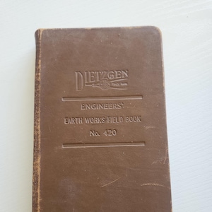 May include: A brown leather-bound book with the title "Engineers' Earth Works Field Book No. 420" and the embossed logo "E. Dietzgen Co.  Trade Mark" on the front cover.