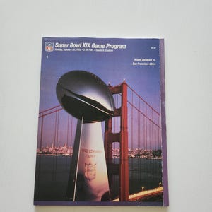 May include: Super Bowl XIX Game Program from 1985. The cover features the Vince Lombardi Trophy, the Golden Gate Bridge, and the Miami Dolphins vs. San Francisco 49ers game details.