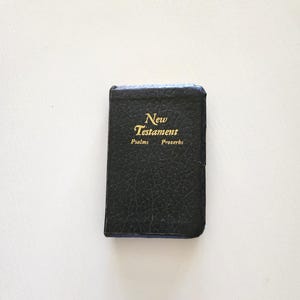 May include: A small, black leather-bound book with gold lettering that reads "New Testament Psalms Proverbs." The book has a blue edge and appears to be a pocket-sized edition.