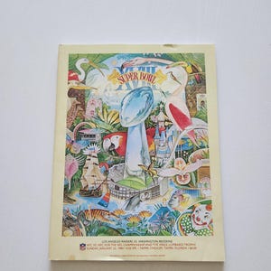 May include: A vintage Super Bowl program cover featuring a colorful illustration. The artwork includes a football trophy, a ship, a parrot, and a flamingo. Text at the bottom lists the teams, date, time, and location of the game.