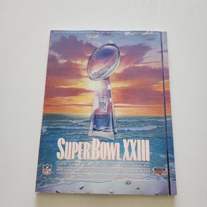 May include: A Super Bowl XXIII commemorative poster featuring the Vince Lombardi Trophy. The poster has a sunset background with the words "Super Bowl XXIII" in large letters. The NFL logo is visible.