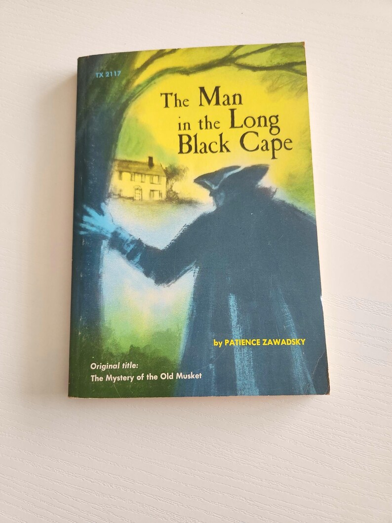 Pode incluir: Uma capa de livro com uma ilustra&ccedil;&atilde;o amarela, verde e azul de um homem com uma capa preta em p&eacute; em frente a uma casa. O t&iacute;tulo do livro &eacute; "The Man in the Long Black Cape" de Patience Zawadsky. O t&iacute;tulo original &eacute; "The Mystery of the Old Musket".