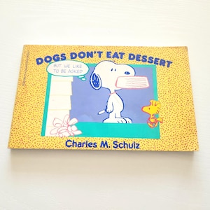 May include: A children's book titled "DOGS DON'T EAT DESSERT" featuring Snoopy holding a dessert dish. The cover has a yellow background with small dots and a blue and green illustration. The author's name, Charles M. Schulz, is also visible.