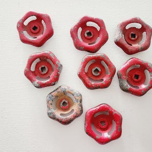 May include: Eight red metal knobs with a hexagonal shape and a circular hole in the center. The knobs have a worn, distressed look, with some rust and scratches.