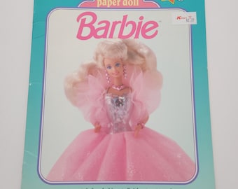 May include: A vintage "Deluxe Paper Doll Barbie" book. The cover shows a Barbie doll in a pink gown with a turquoise border. The text includes "More Fashions!" and "more precut clothes fashions to finish storage envelope".