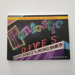 May include: A yellow and black book cover with the title "Fantastic Dives" in neon-colored letters. The book is a guide to LA's best hole-in-the-wall dining by Elliott Korentz and Michael Nankin.