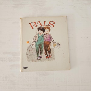 May include: Vintage children's book titled "Pals" featuring an illustration of two boys walking together. The cover art shows the boys in colorful clothing, with the word "Pals" in red lettering. The book is on a white surface.