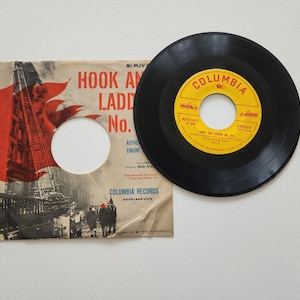 May include: A vintage 45 RPM record and sleeve. The record is black with a yellow and red label that reads "Columbia". The sleeve features a red and black illustration of a fire truck and the text "Hook and Ladder No. 9".