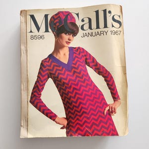 May include: Vintage McCall's sewing pattern cover from January 1967. The cover features a woman wearing a red and purple chevron-patterned dress and matching hat. The text "McCall's" is at the top, with the issue number and date below.