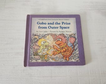 May include: A vintage children's book titled "Gobo and the Prize from Outer Space" featuring illustrations of two cartoon characters. The book has a purple cover with the title in white and the authors' names. The book is from the Fraggle Rock series.