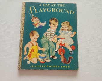 Puede incluir: Libro infantil vintage titulado "A Day at the Playground". La portada presenta ilustraciones de niños jugando, incluyendo un columpio, un triciclo y una ardilla. El libro tiene un fondo turquesa con letras doradas y un lomo dorado.