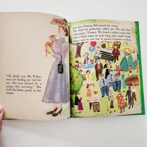 Może przedstawiać: Antyczna książka dla dzieci otwarta na stronie z ilustracją kobiety trzymającej kociaka. Tekst na stronie brzmi: "Och, dziękuję, panie policjancie, za odnalezienie mojego zaginionego kociaka. Był ścigany przez szczeniaka tego ranka." Ona wzięła kociaka delikatnie w swoje ręce. Przeciwległa strona przedstawia ilustrację tłumu ludzi, w tym policjant&oacute;w, dzieci i zwierząt.