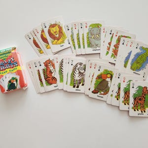 May include: A deck of Crazy Eights card game cards with animal illustrations, including a lion, elephant, tiger, zebra, toucan, alligator, and giraffe. The card game box is red and green.