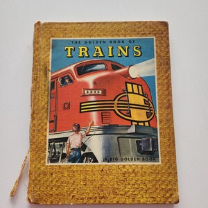 May include: Vintage children's book titled "The Golden Book of Trains." The cover features a red train with the number 2333, a boy waving, and the text "TRAINS" on a blue background. The book has a woven, textured cover.