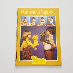 May include: A vintage spiral-bound book titled "Fun with Puppets" with a yellow cover. The cover features illustrations of children with puppets and the text "CREATE ALL KINDS OF PUPPETS". The book is from "Crafts from Current".