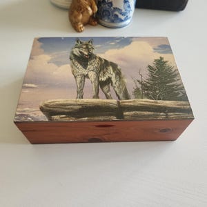 May include: A wooden box with a hinged lid. The lid features a colorful image of a wolf standing on a rock with a forest background.