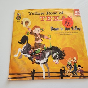 May include: A vintage record sleeve featuring a cartoon illustration of a girl riding a horse. The sleeve is yellow with red and white text that reads "Yellow Rose of Texas" and "Down in the Valley".