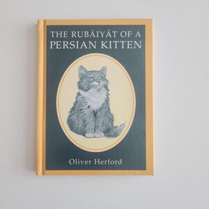 May include: A hardcover book titled "THE RUBÁIYÁT OF A PERSIAN KITTEN" by Oliver Herford. The cover features a pencil sketch of a gray and white Persian cat inside an oval on a dark green background with a gold border.
