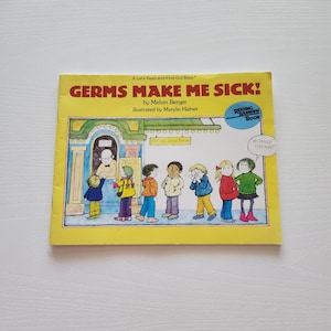 May include: A children's book titled "GERMS MAKE ME SICK!" by Melvin Berger, illustrated by Marylin Hafner. The cover is yellow with illustrations of children and a building. The book is part of the "Reading Rainbow Book" series.
